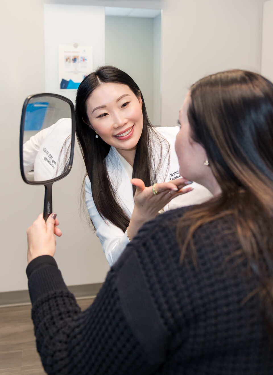 Dermatologist consulting a patient, reviewing facial results in a hand mirror during cosmetic skin treatment.