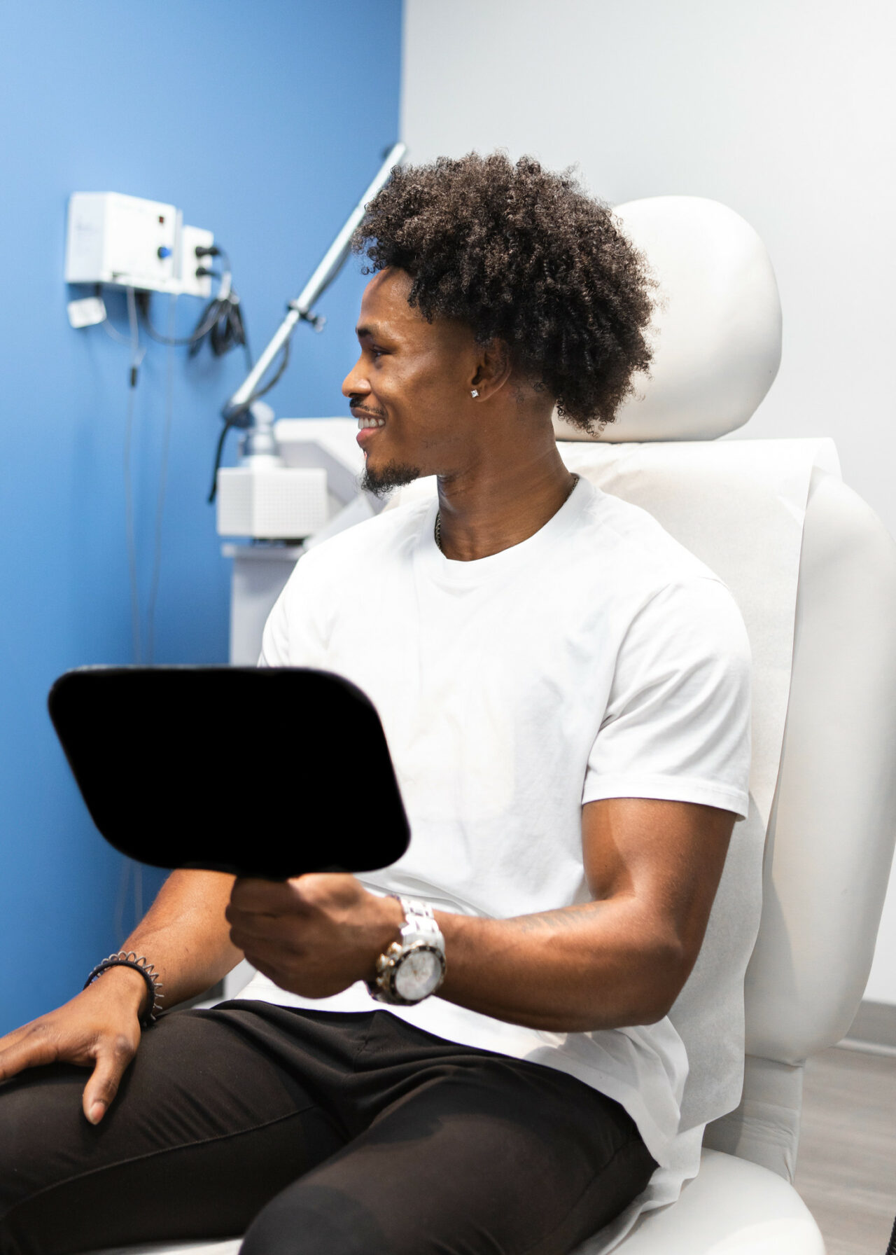 A male patient in dermatology clinic holding a mirror, smiling after injectable skincare consultation in Birmingham, AL