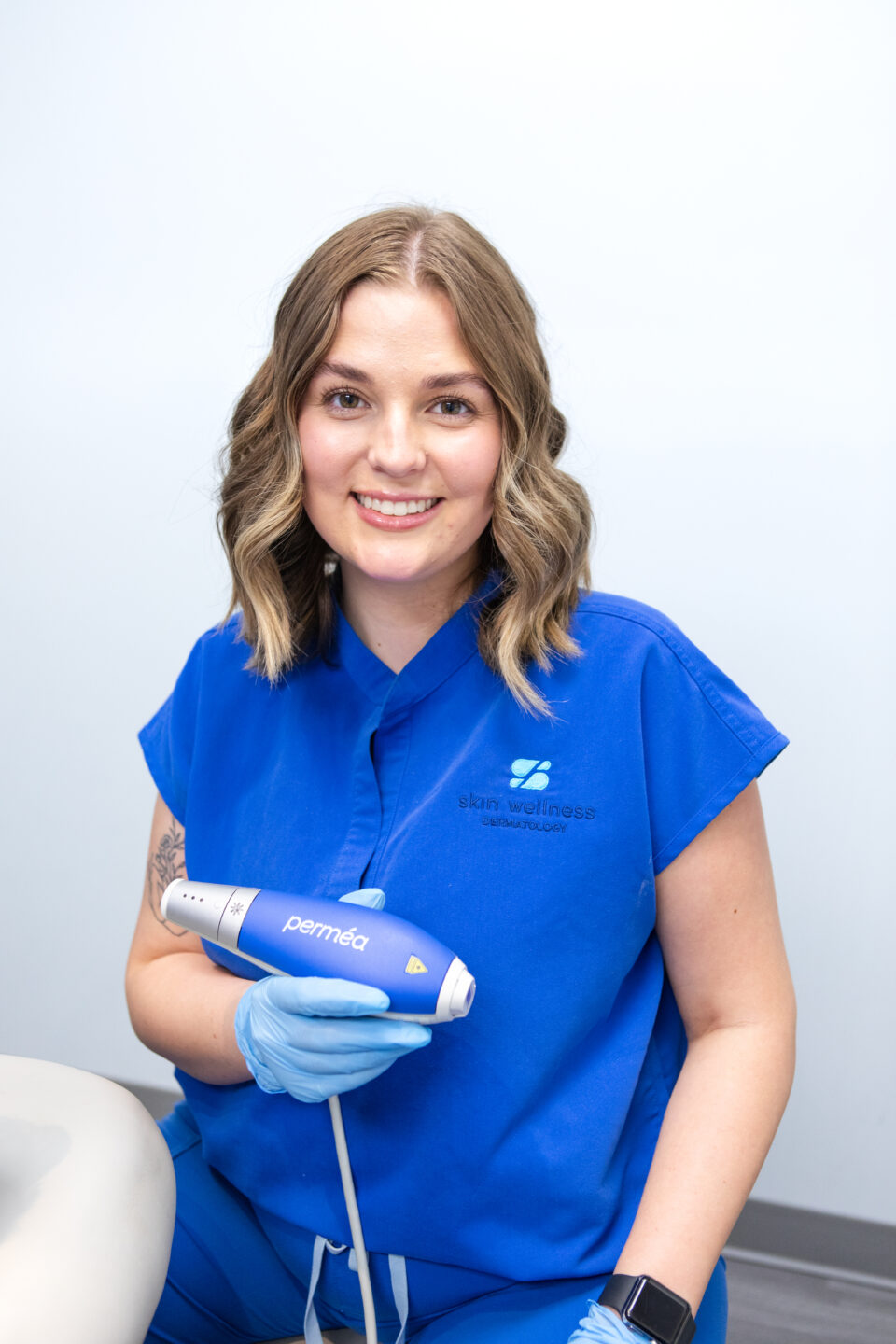 Woman in blue scrubs holding a Permeá skin treatment device in a dermatology clinic