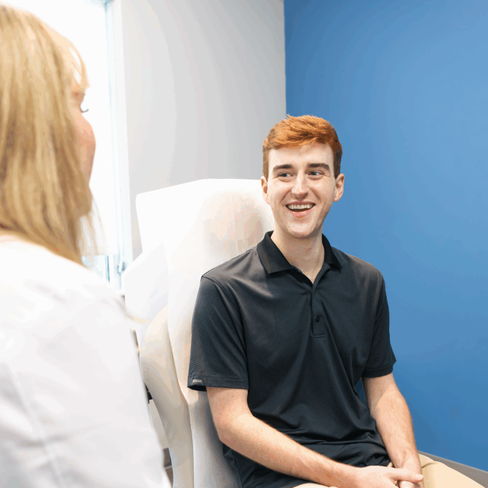 A man smiling in a dermatology clinic chair during a consultation with a clinician