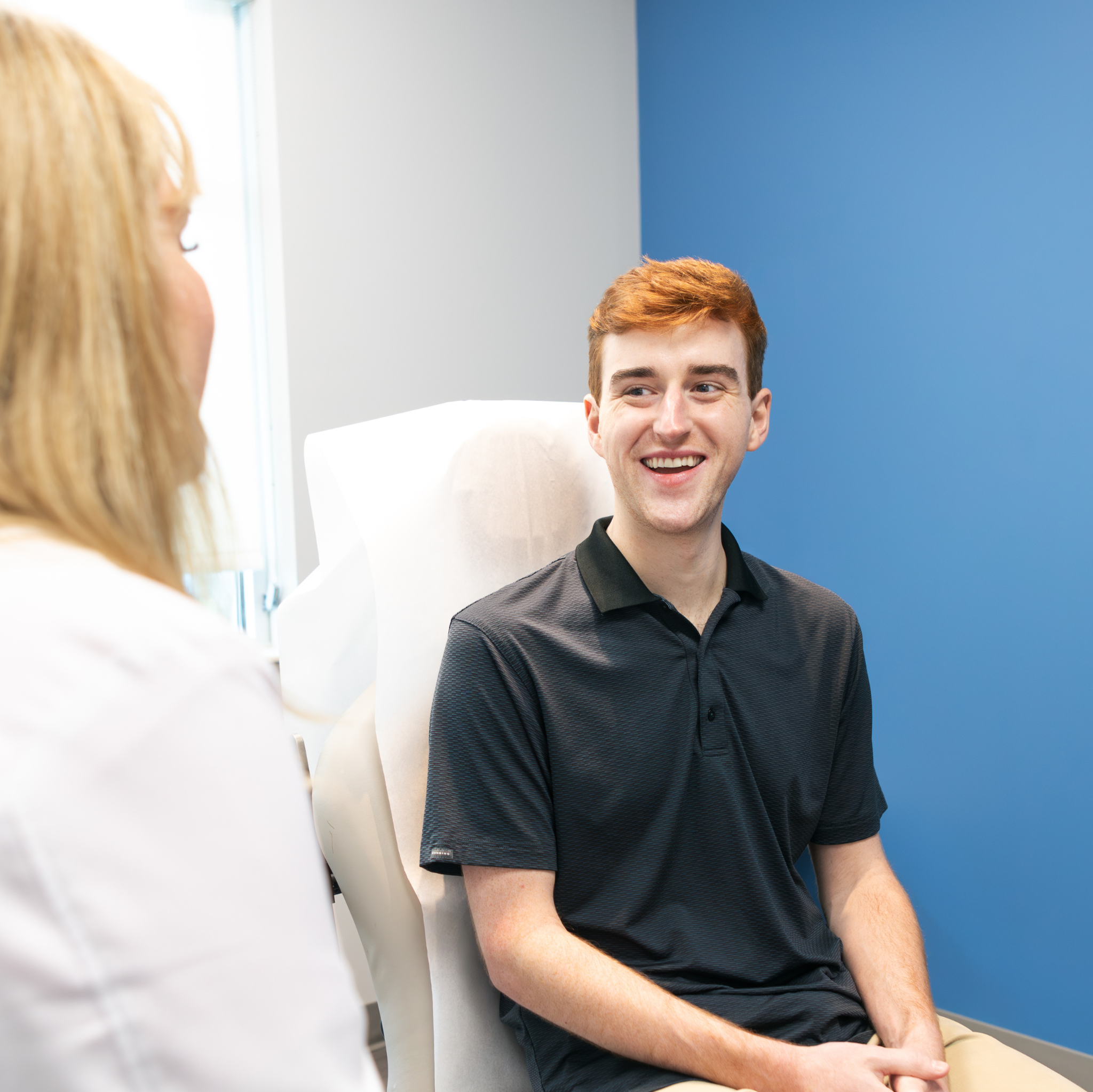 A man smiling in a dermatology clinic chair during a consultation with a clinician