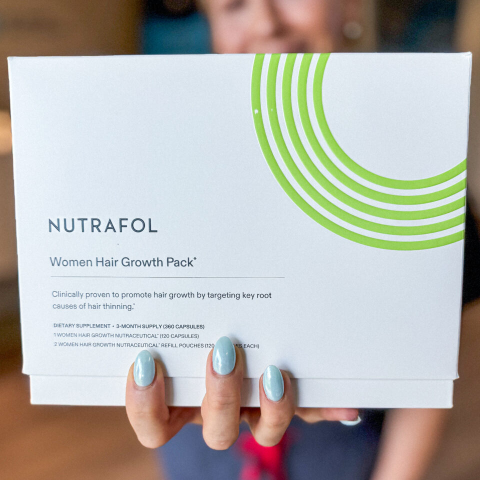A woman holding a Nutrafol Women Hair Growth Pack box, close-up of packaging and light blue manicured nails.