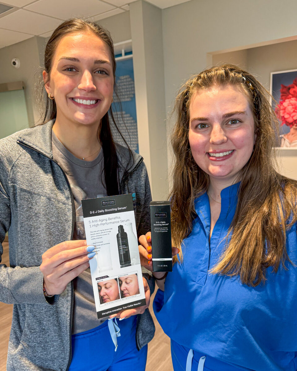 Two women holding Revision Skincare DEJ Daily Boosting Serum brochure and box in Birmingham dermatology clinic