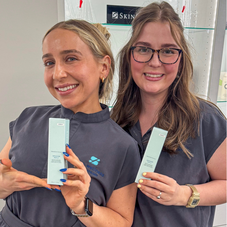 Two smiling skincare staff holding boxed serums in a Birmingham dermatology clinic, wearing gray uniforms.