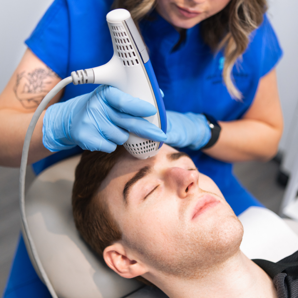 Dermatology clinician using handheld laser on a man's forehead for facial skin treatment.