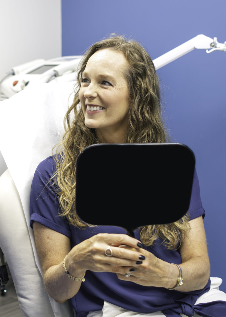 A woman patient smiling and holding a mirror at a Birmingham dermatology clinic after a skin treatment