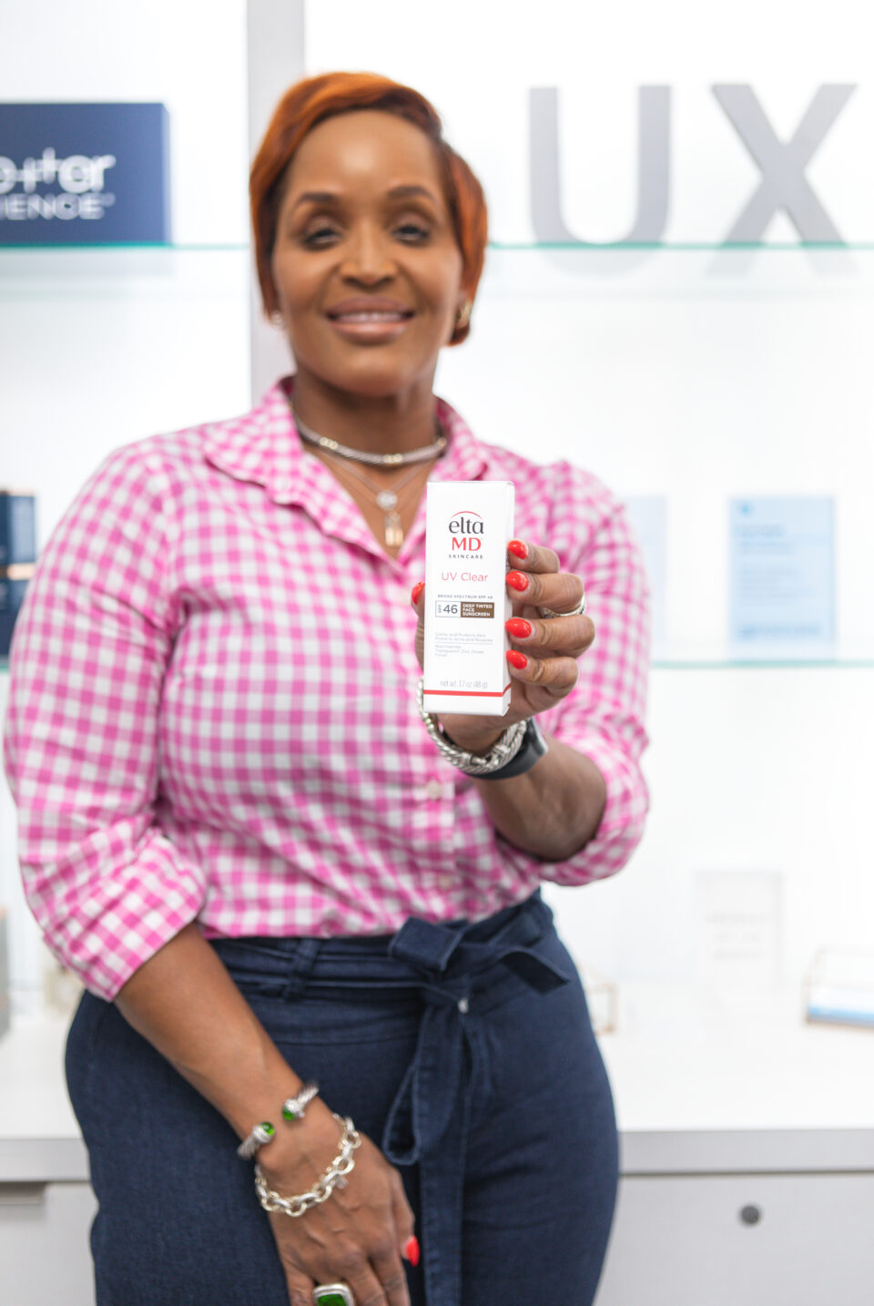 Woman in pink gingham holds EltaMD UV Clear SPF 46 sunscreen in dermatology clinic