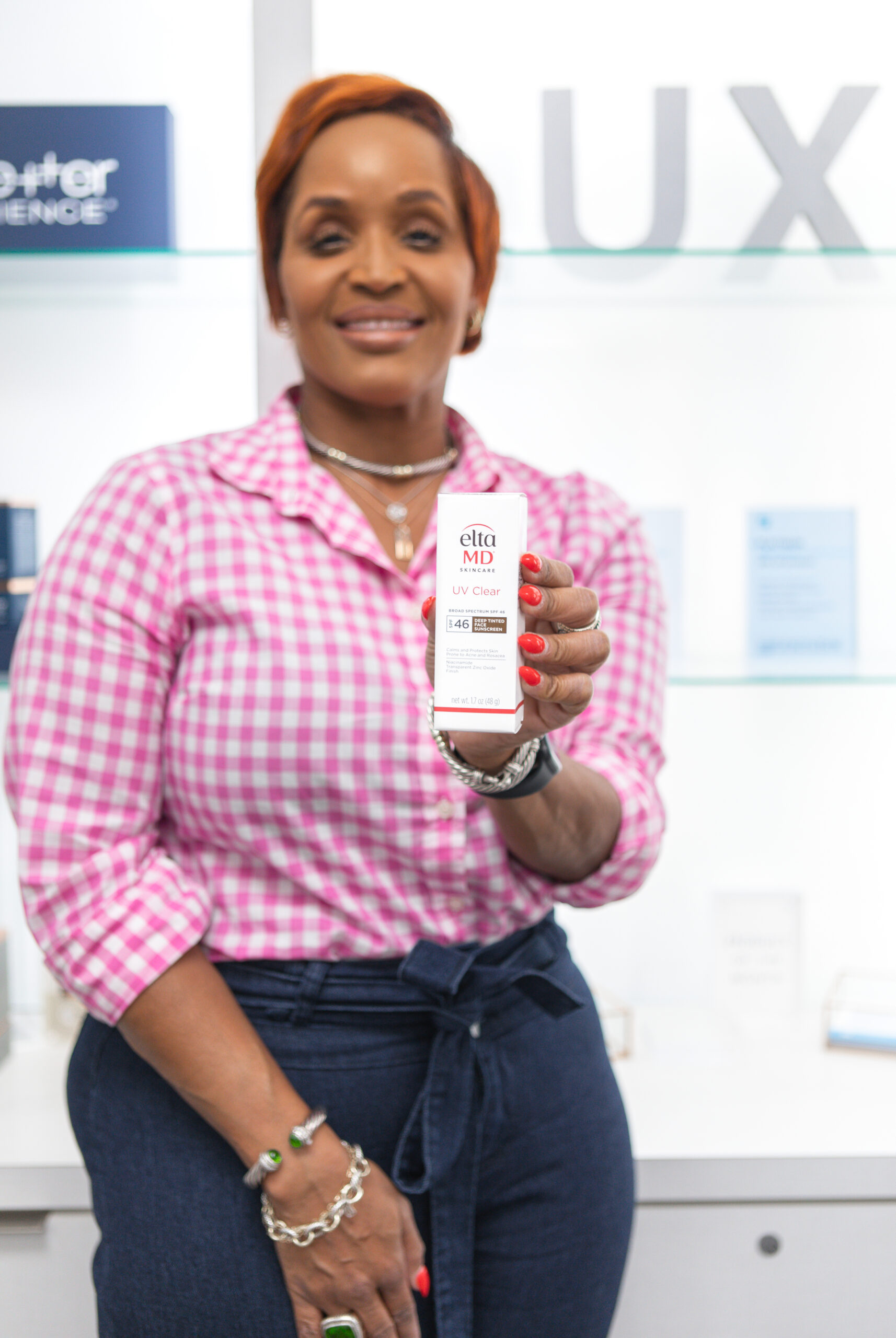 Woman in pink gingham holds EltaMD UV Clear SPF 46 sunscreen in dermatology clinic
