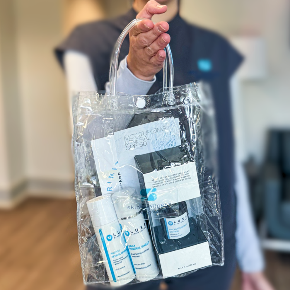 A person holding a clear bag of skincare products, including Moisturizing Mineral SPF 50 and Daily Mineral Shield.