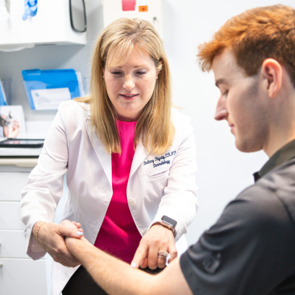 A doctor in a dermatology clinic examining a patient's forearm during a skin-care consultation
