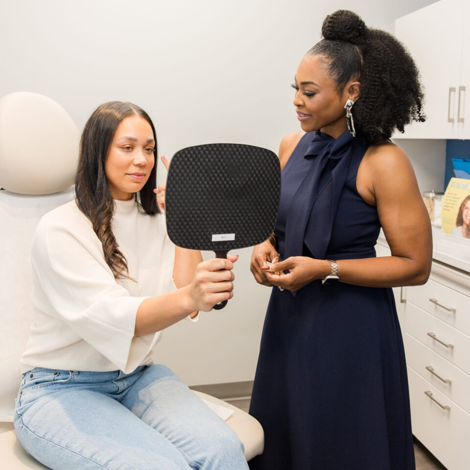 A patient holding a mirror during cosmetic dermatology consultation with a clinician in a skincare clinic.