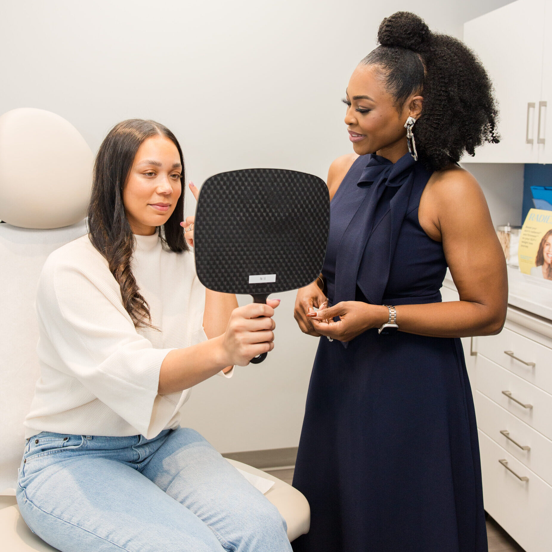 A patient holding a mirror during cosmetic dermatology consultation with a clinician in a skincare clinic.