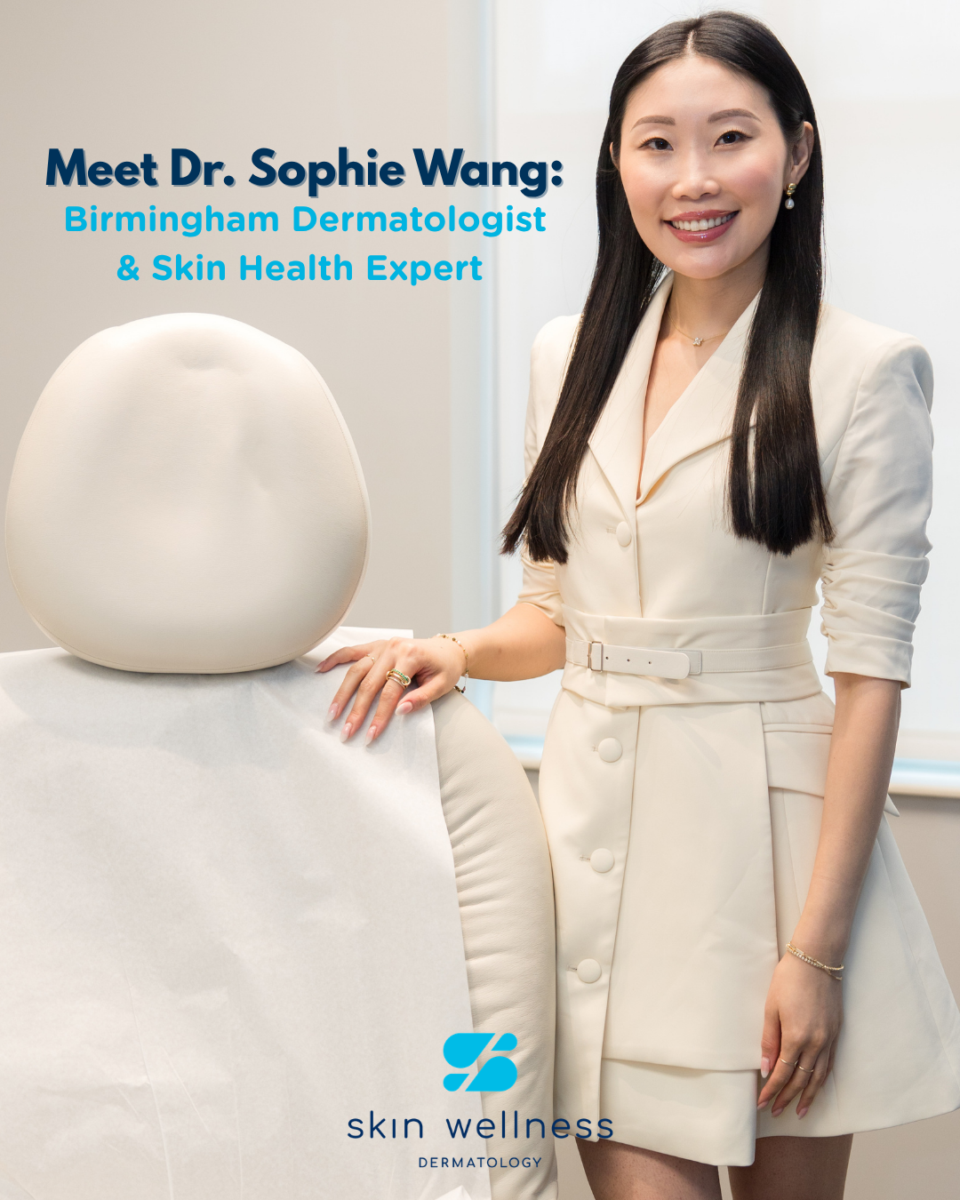 Woman dermatologist in cream suit smiling beside exam chair in Birmingham skin wellness office