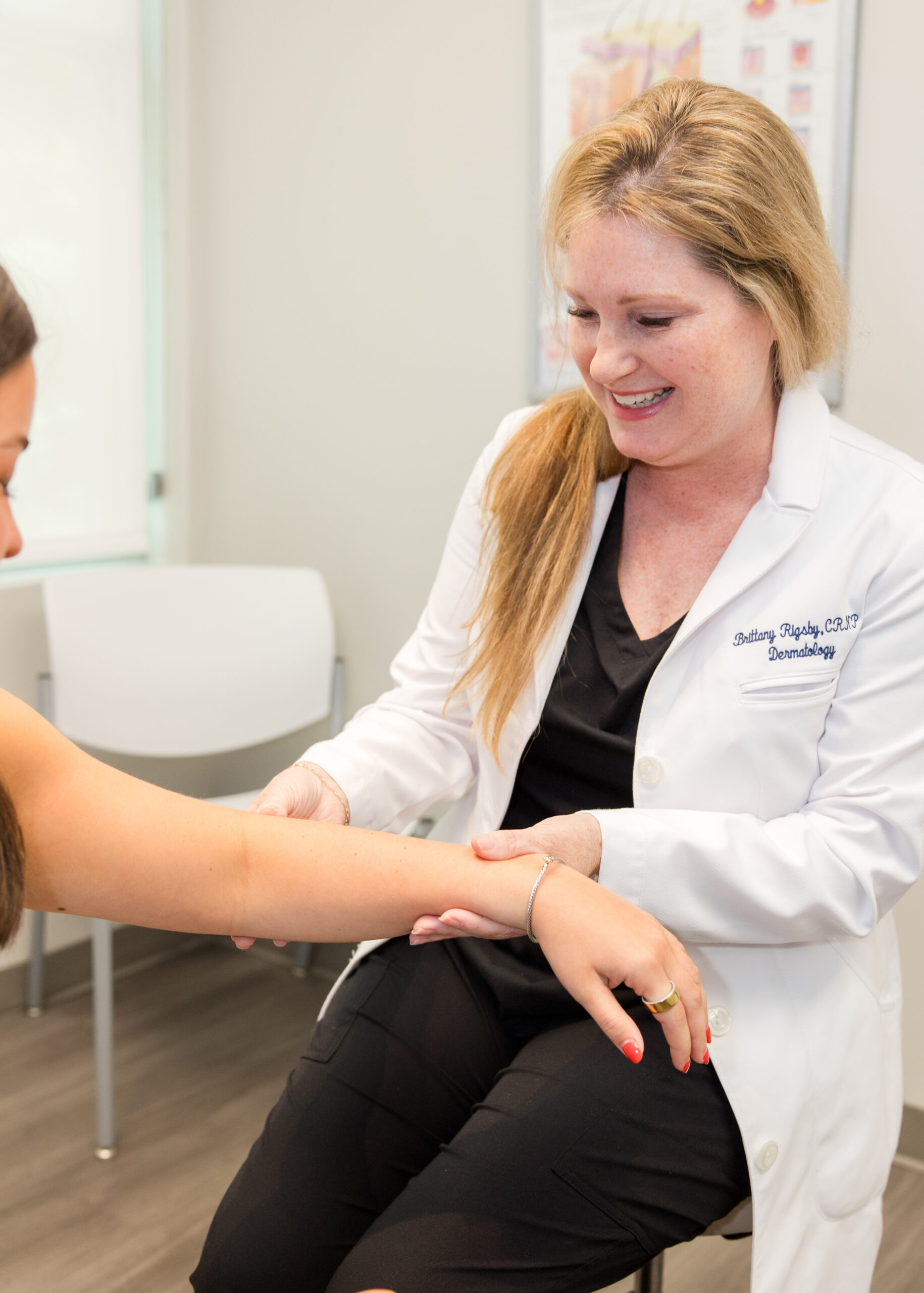 A doctor in a white coat examining a patient's forearm, smiling in a dermatology clinic
